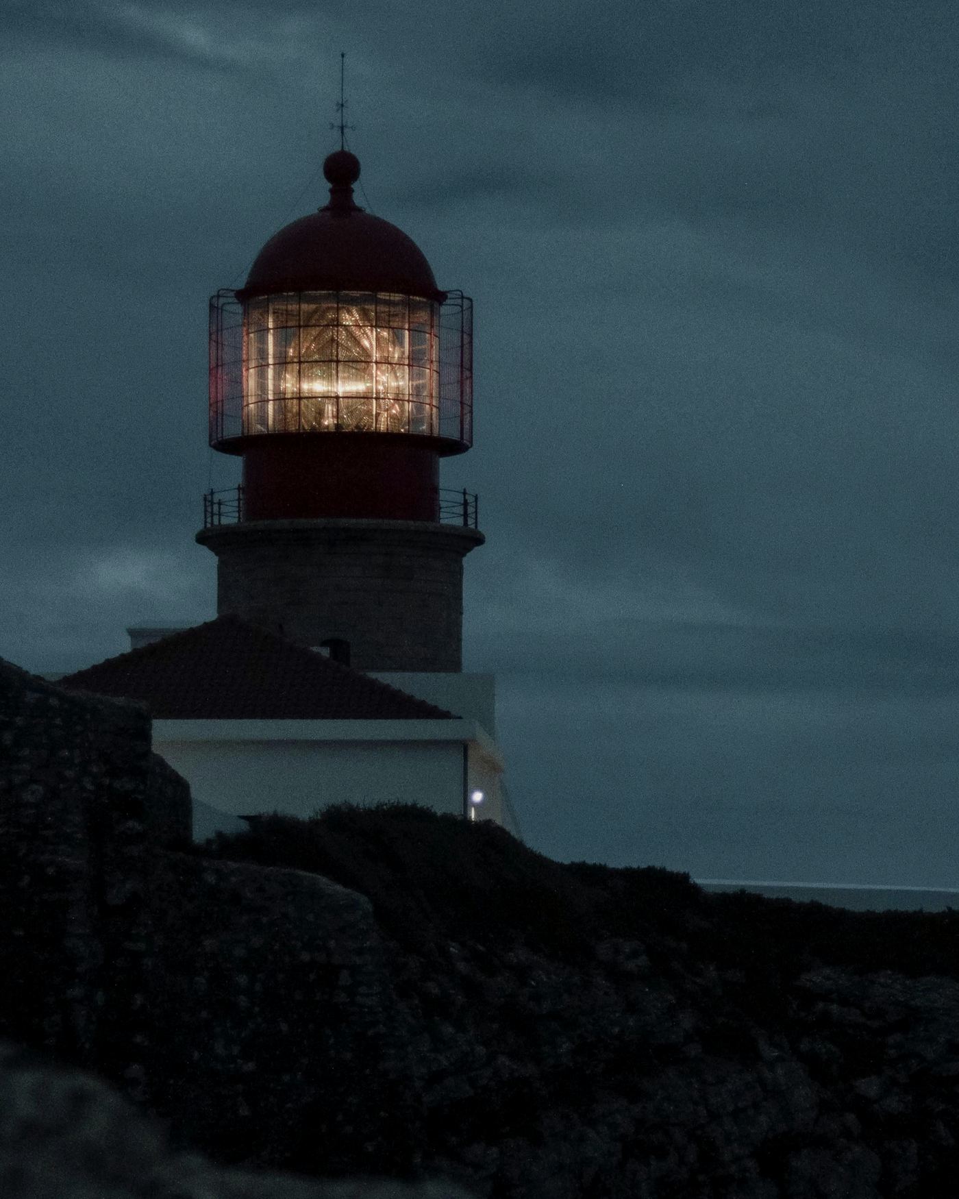 A lighthouse lit at dusk above dark rocks